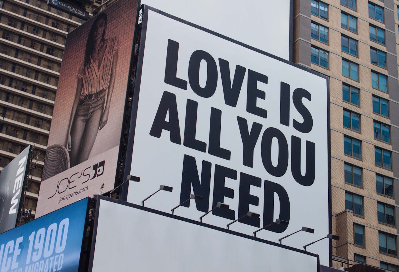 Large city billboard reads 'Love Is All You Need' in New York City street.